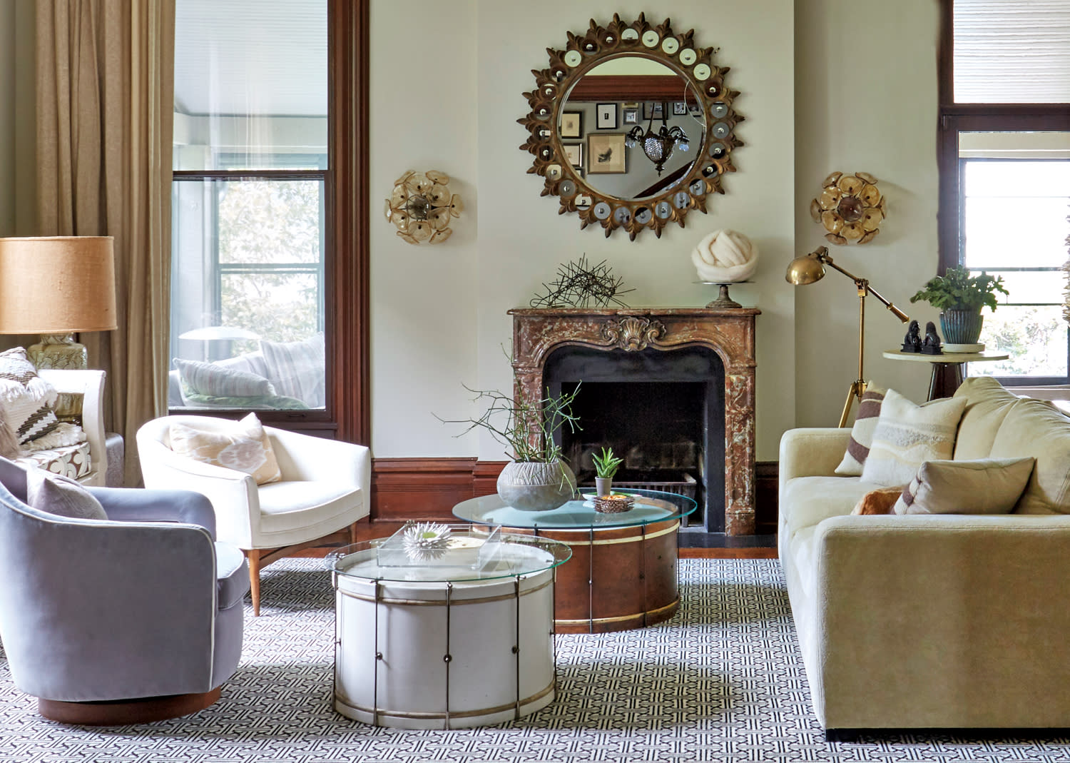 Living room with circular coffee tables, ornate sunburst mirror and a stone fireplace.