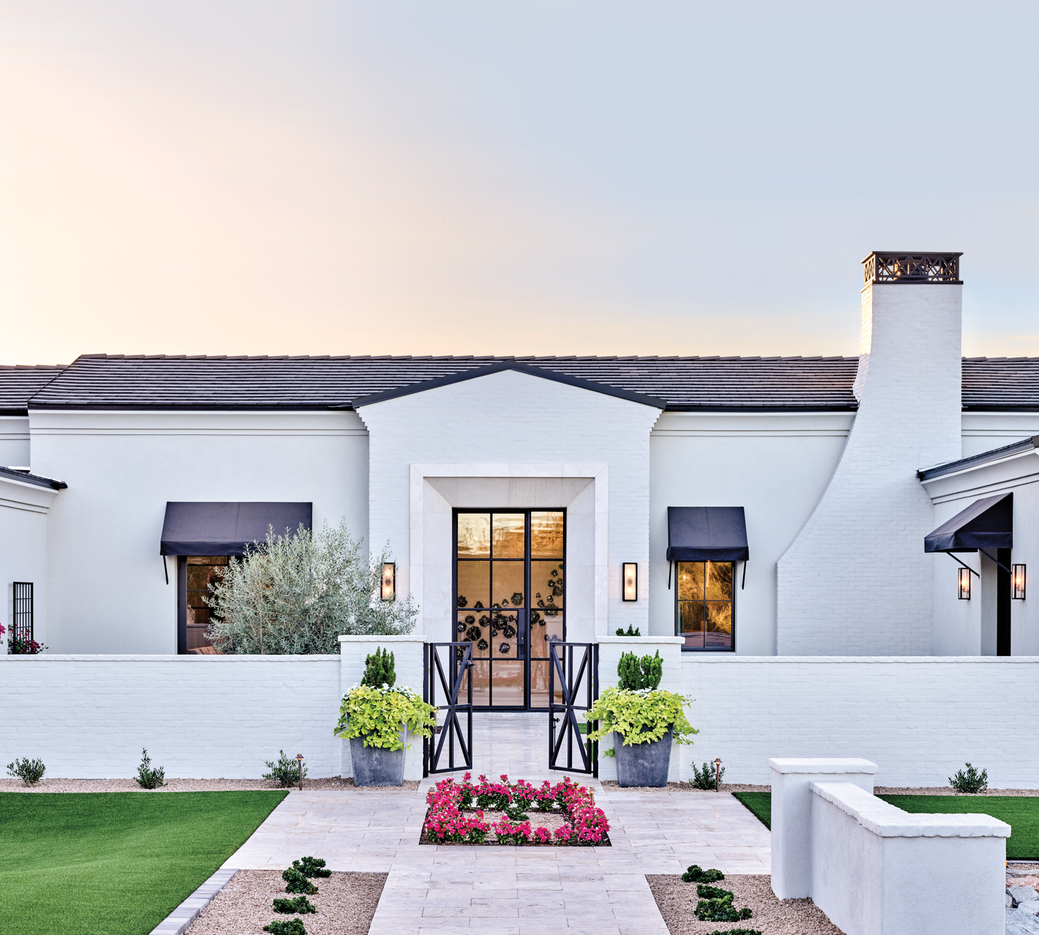 The front facade of a white brick house with a gate and a steel-and-glass entry door.