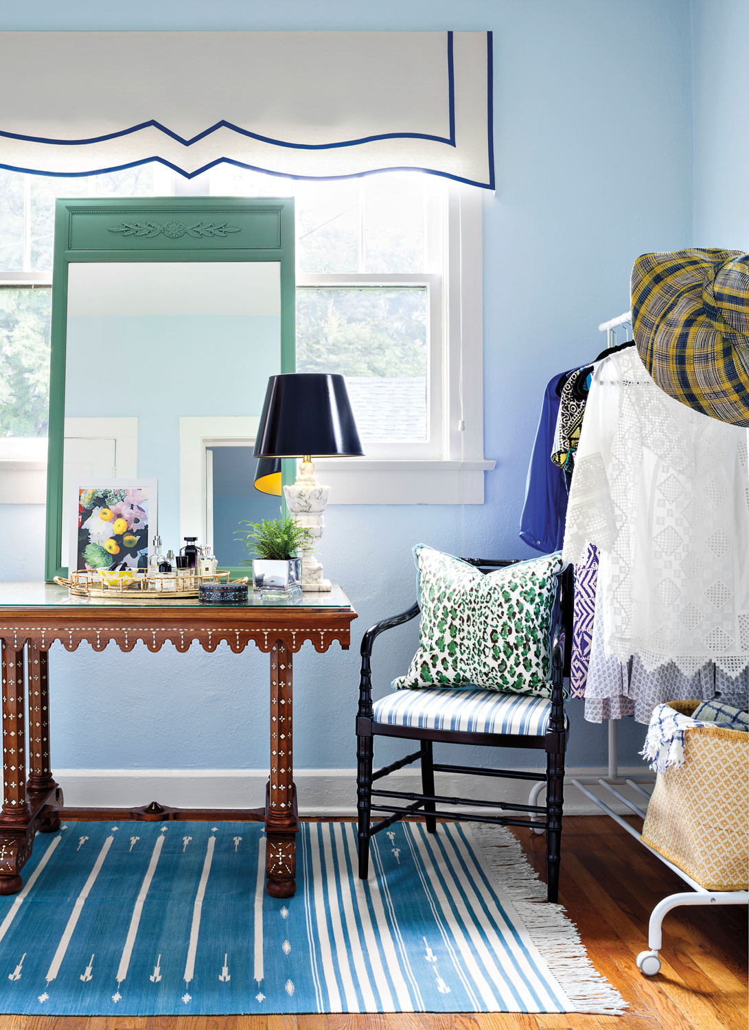 A chair with a patterned-pillow on top sitting next to a console table with a scalloped edge.