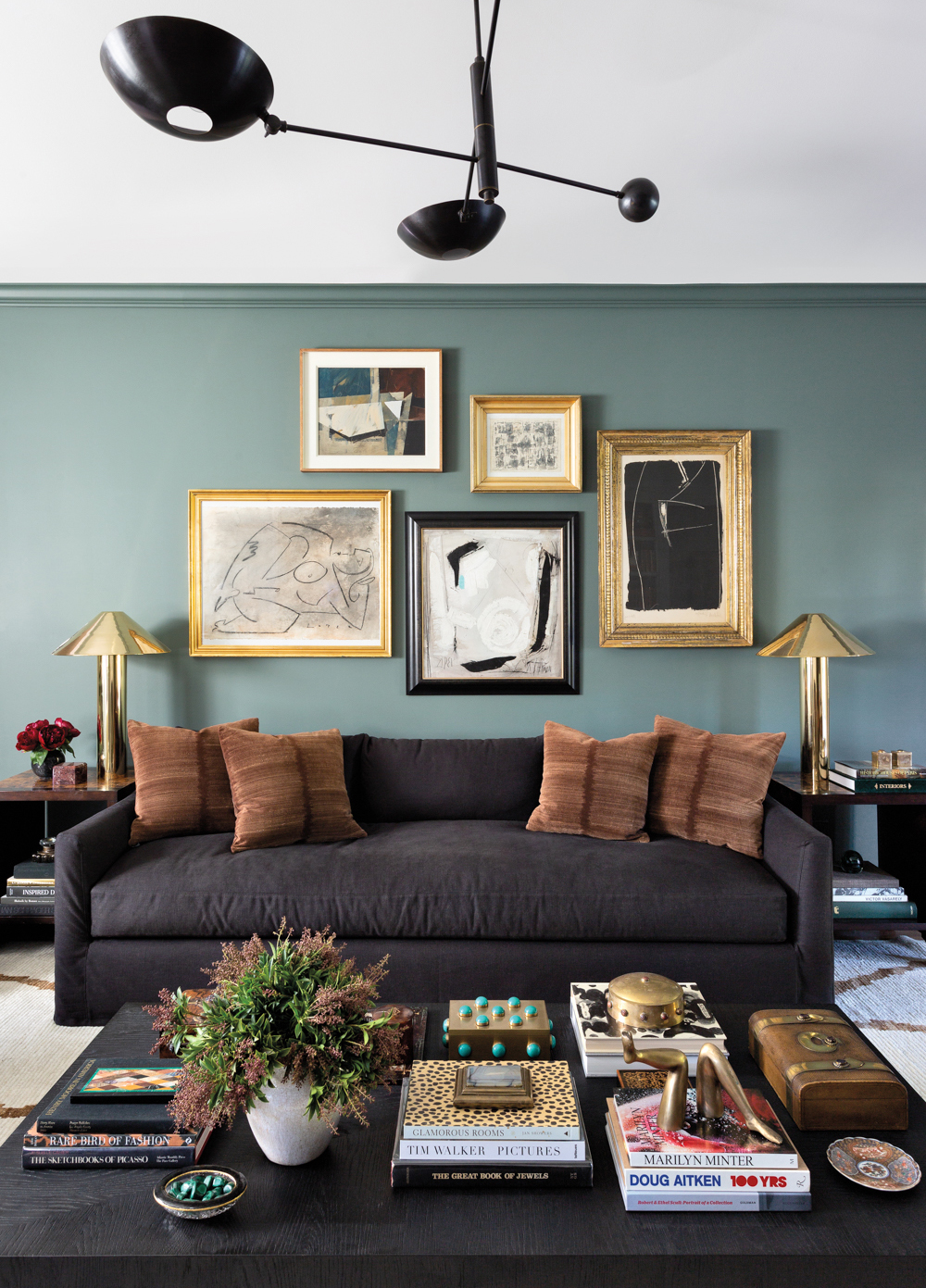 black couch with tan pillows and a coffee table, backed by a sage green painted wall and antique paintings