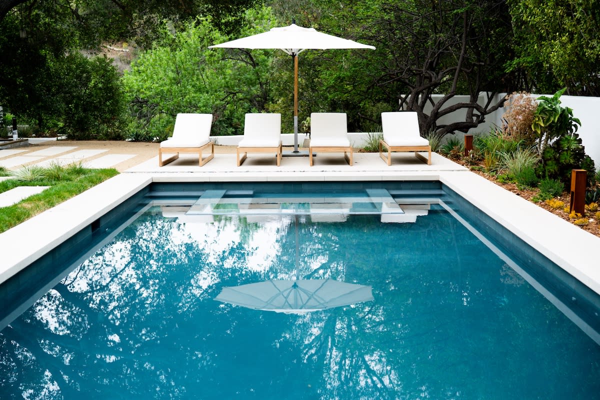 A serene poolside scene featuring lounge chairs and a large umbrella for shade.