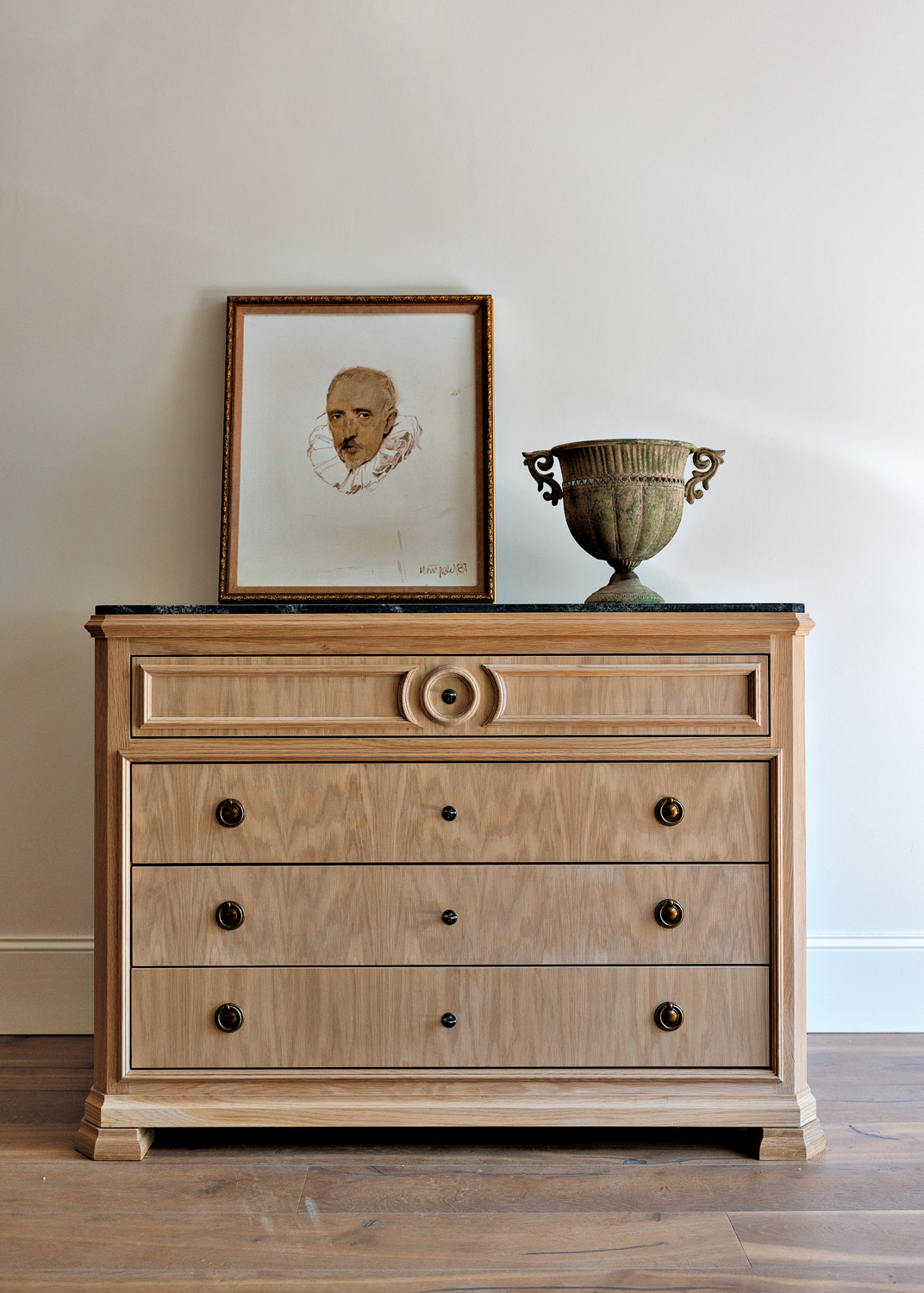 Light wood dresser with artwork and decorative vessel sitting atop.