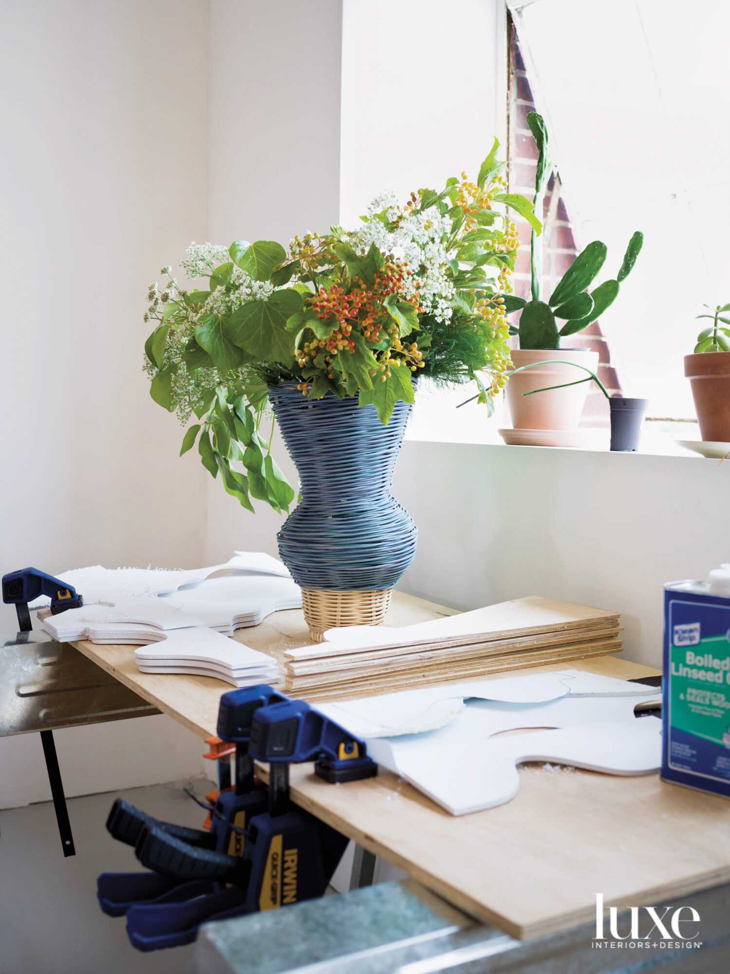 A blue basket vase with flowers on a work table.