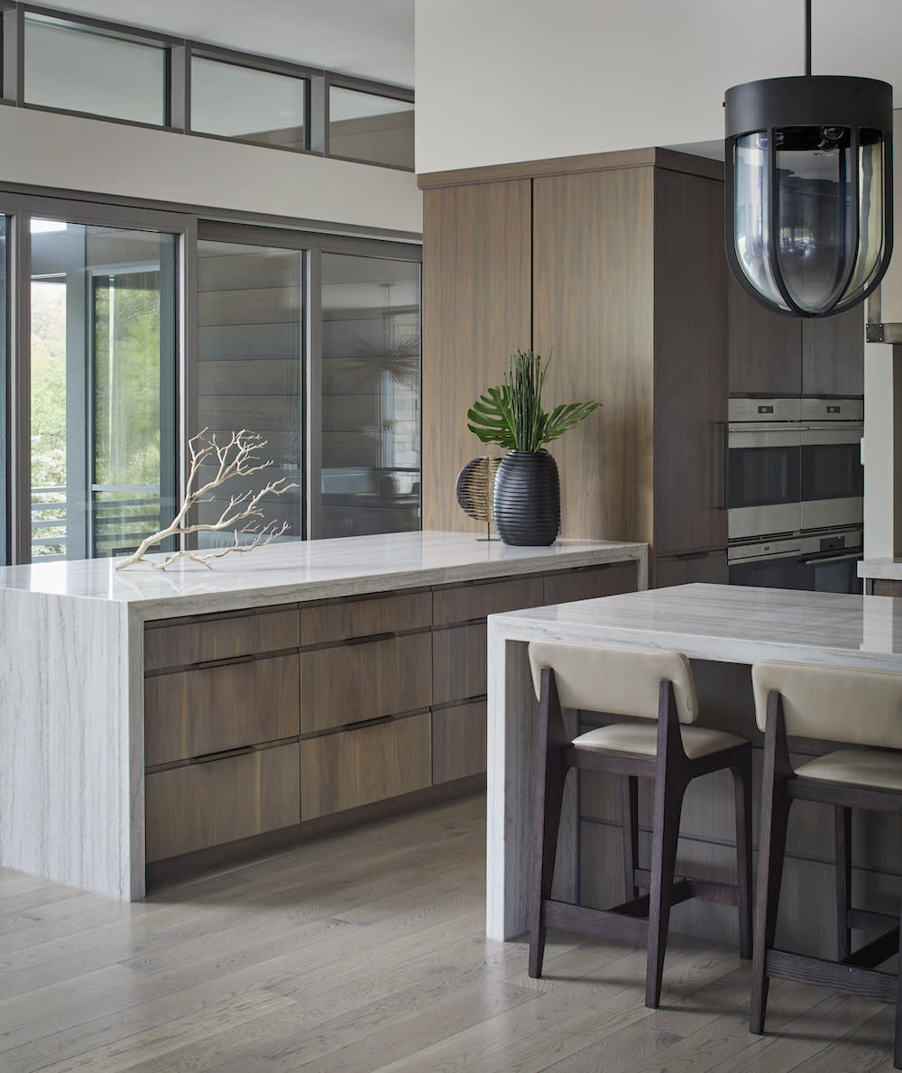 Minimalist kitchen with natural wood cabinets, two white waterfall islands and black decorative accents.