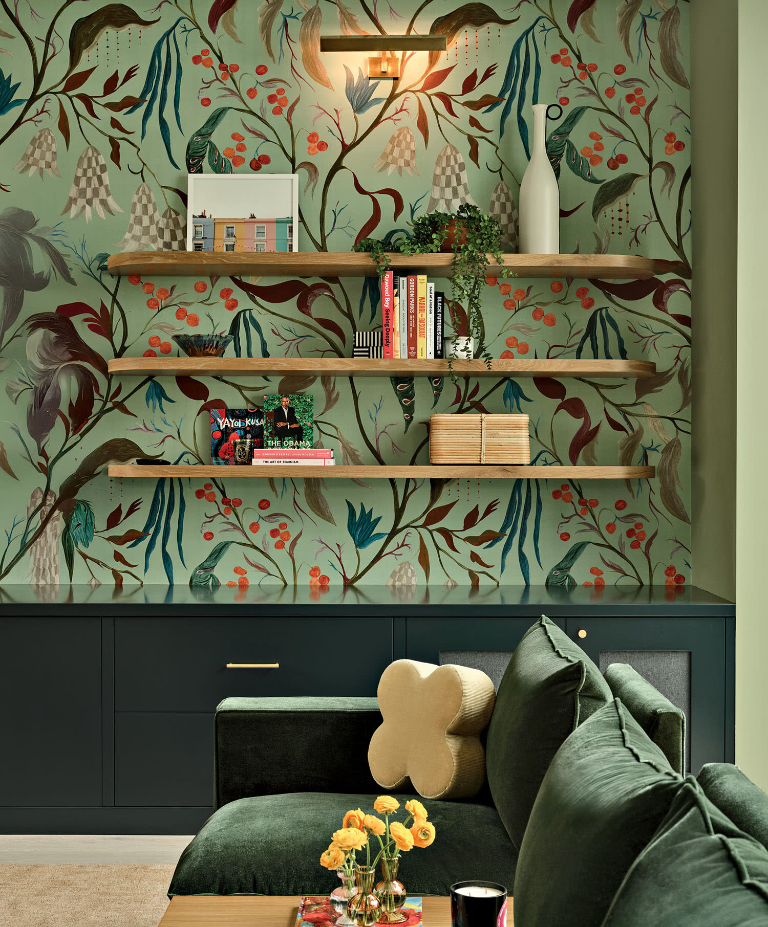 Cozy living room with floral wallpaper, three wooden shelves with books, vases, and decor