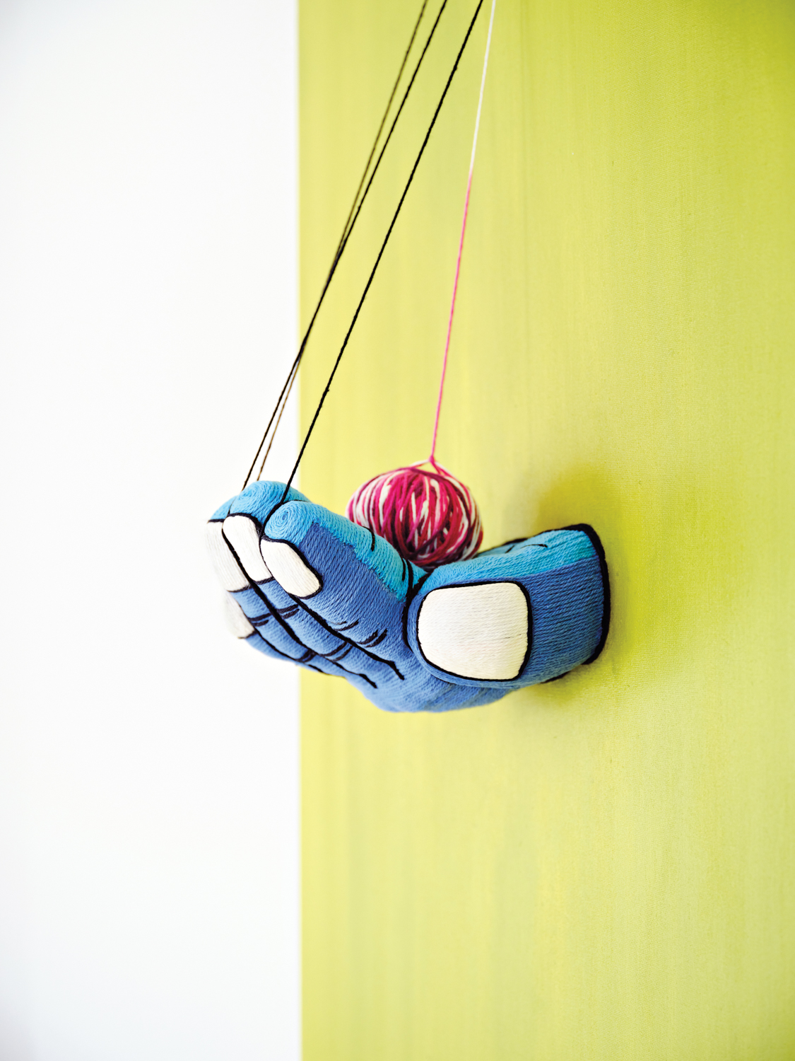 vibrant yarn artwork by michelle drummond showing a blue hand holding a ball against a neon green-yellow background