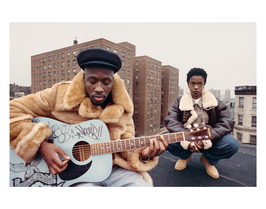 one man with tan coat and guitar sitting next to woman with jacket