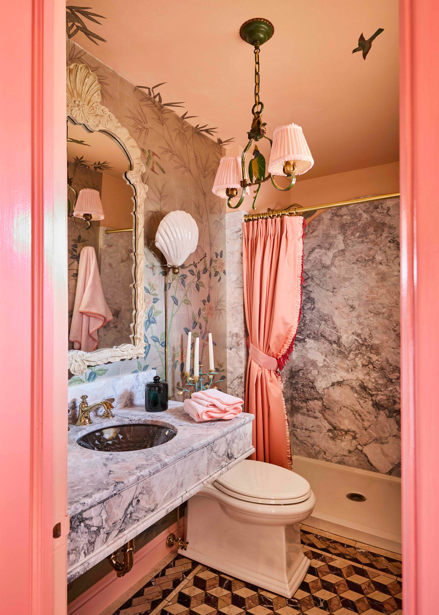 Vintage bathroom with pink pastel walls, a marble countertop, floral wallpaper, a scallop mirror, and coral shower curtain. Elegant, cozy atmosphere.