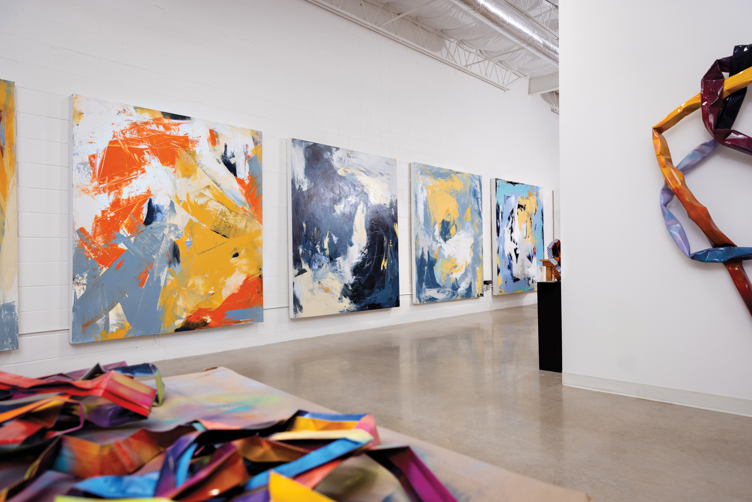 Four colorful abstract paintings in a gallery with concrete floors