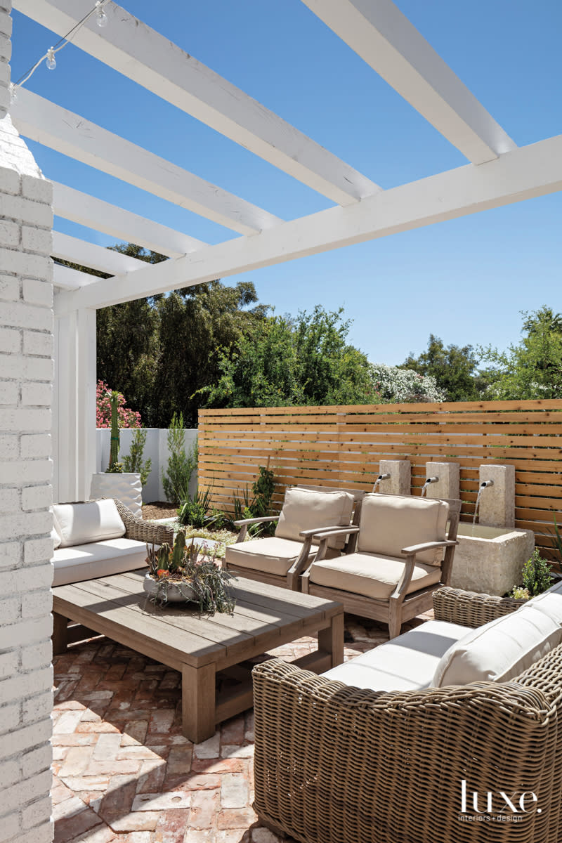 outdoor fireplace area with a sofa and three armchairs under wooden white beams