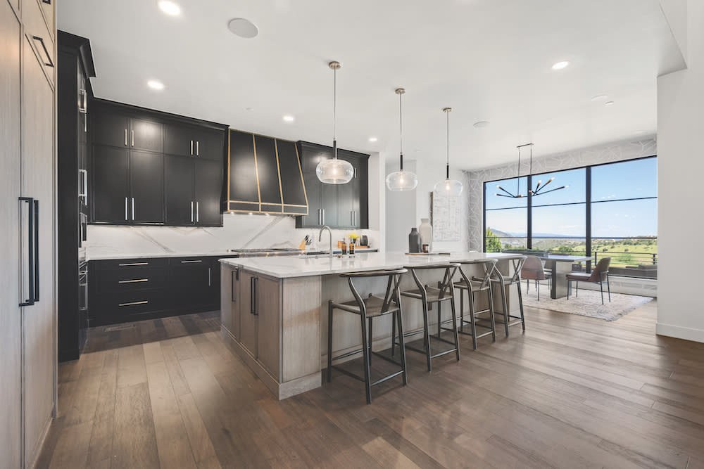 Modern kitchen with black cabinets, gold trim on hood three glass hanging pendant lights above center island.