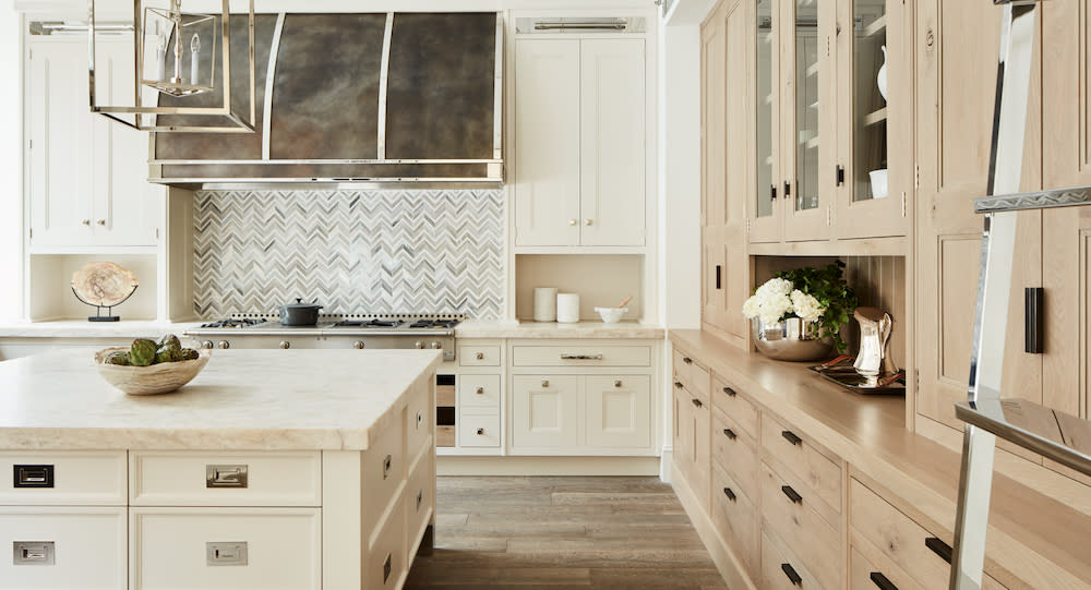 Oak cabinets, large center island with marble counter, chevron patterned backsplash with white and gray tiles.