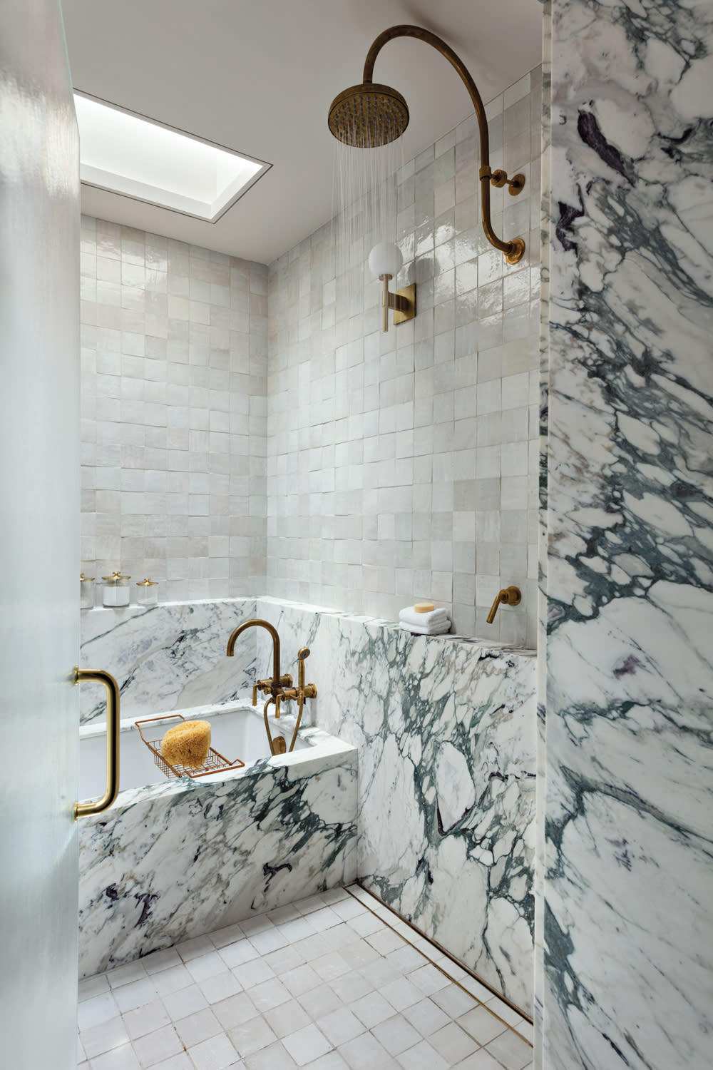 Luxurious bathroom with marble walls, gold fixtures, and a skylight. The modern design conveys elegance and sophistication with a serene tone.