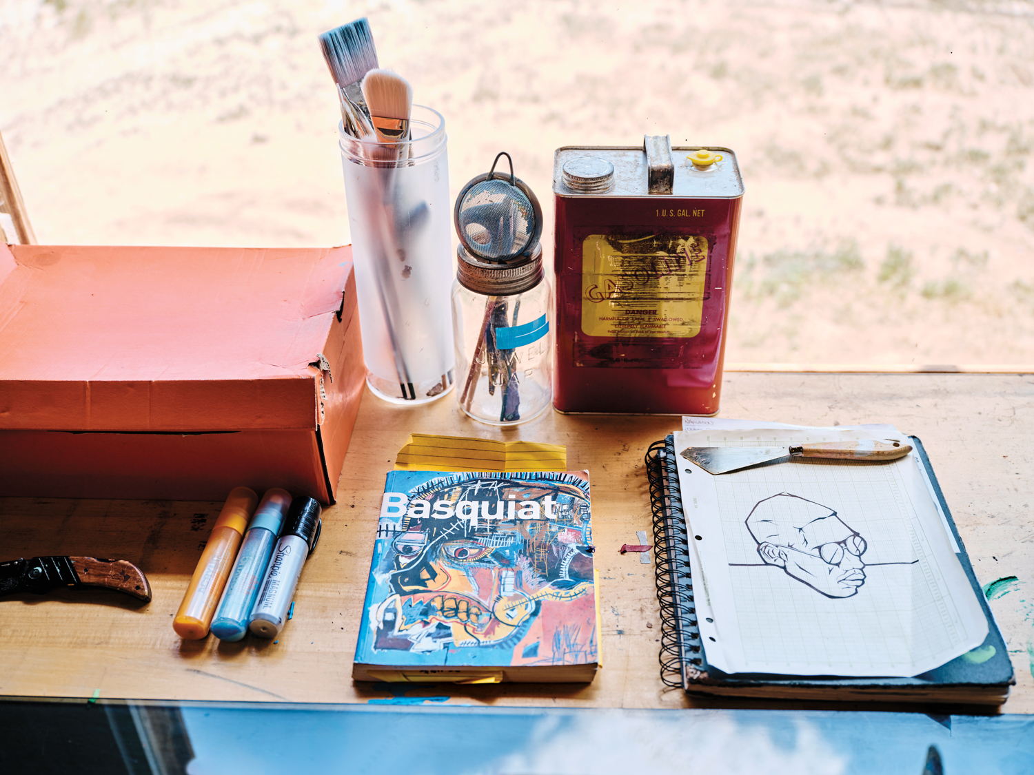 outdoor wooden workbench with sketchbook, art book, pens and paintbrushes