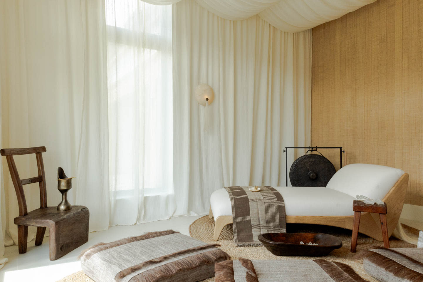 A serene spa room with a minimalist design features a white lounger, draped with a brown throw. 