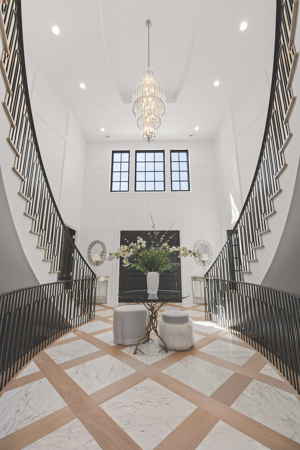 Grand entry way with two staircases, marble floor with light inlaid wood.