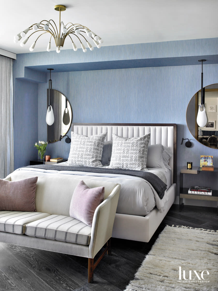 primary bedroom with blue wallcovering, midcentury chandelier, white bed and settee