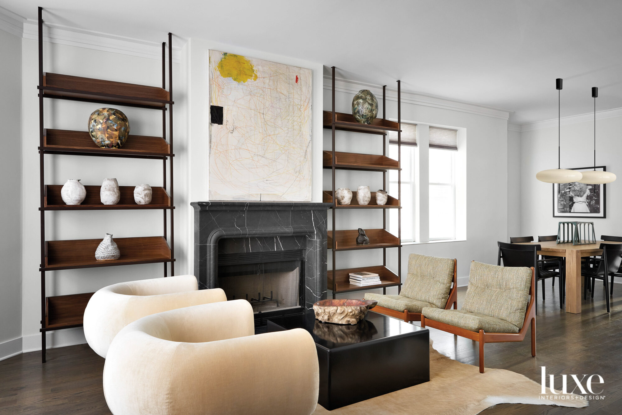 A cocktail area with a black marble fireplace, a pair of curved back chairs and wood open shelving.