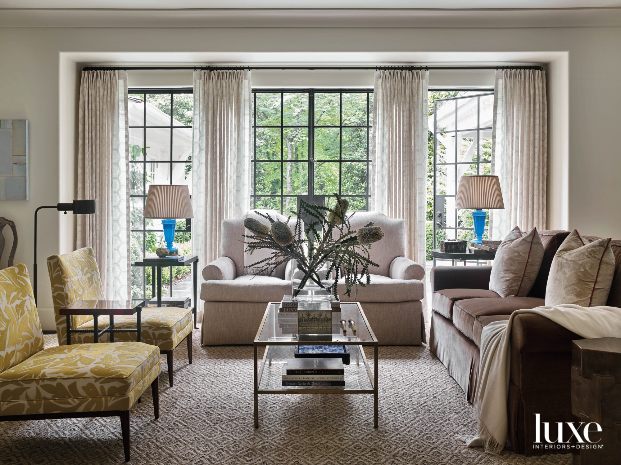 Softly sunlit living room with large windows, cream draperies and several pieces of upholstery