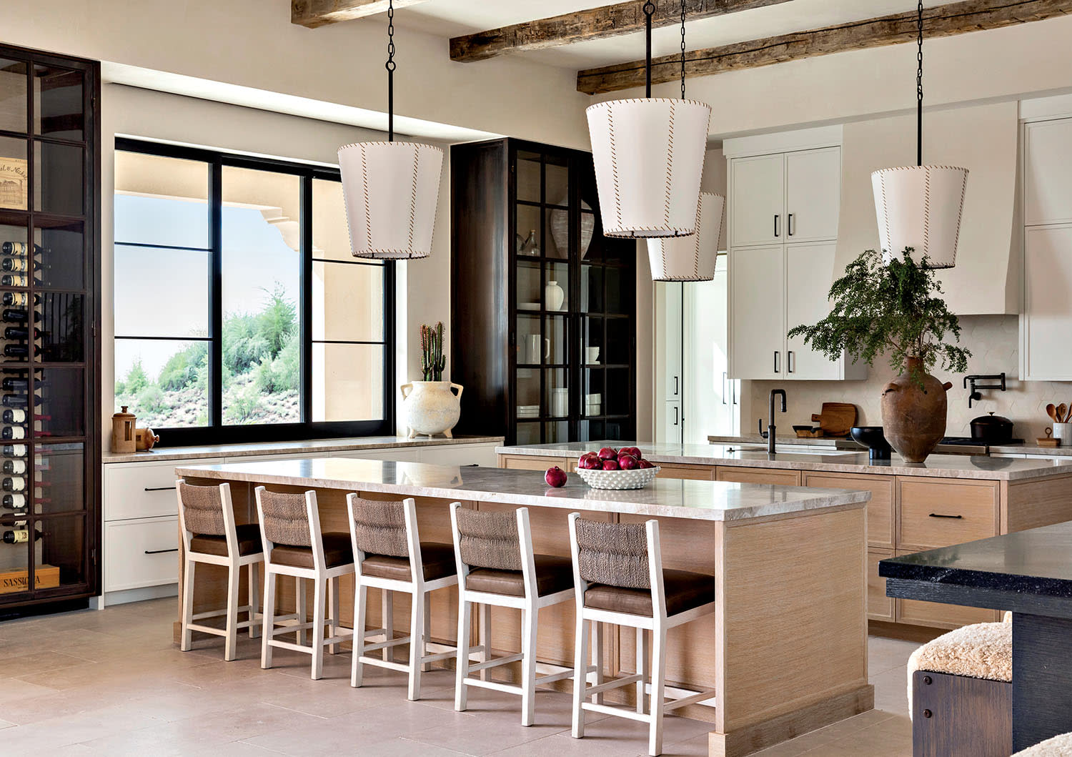 Spacious modern kitchen with a large island, six wooden barstools, and three pendant lights. Bright with natural light from a large window.