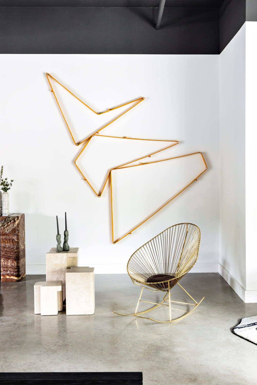 Geometric wall installation behind gold-wired chair and different size stone side tables