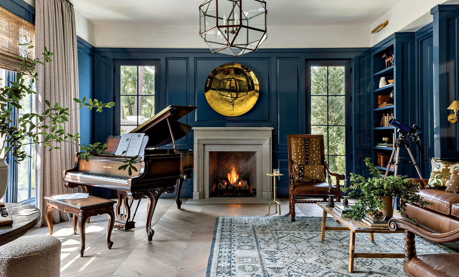 Elegant living room with blue paneled walls, grand piano, and cozy fireplace. Large windows and lush plants add a serene, inviting atmosphere.
