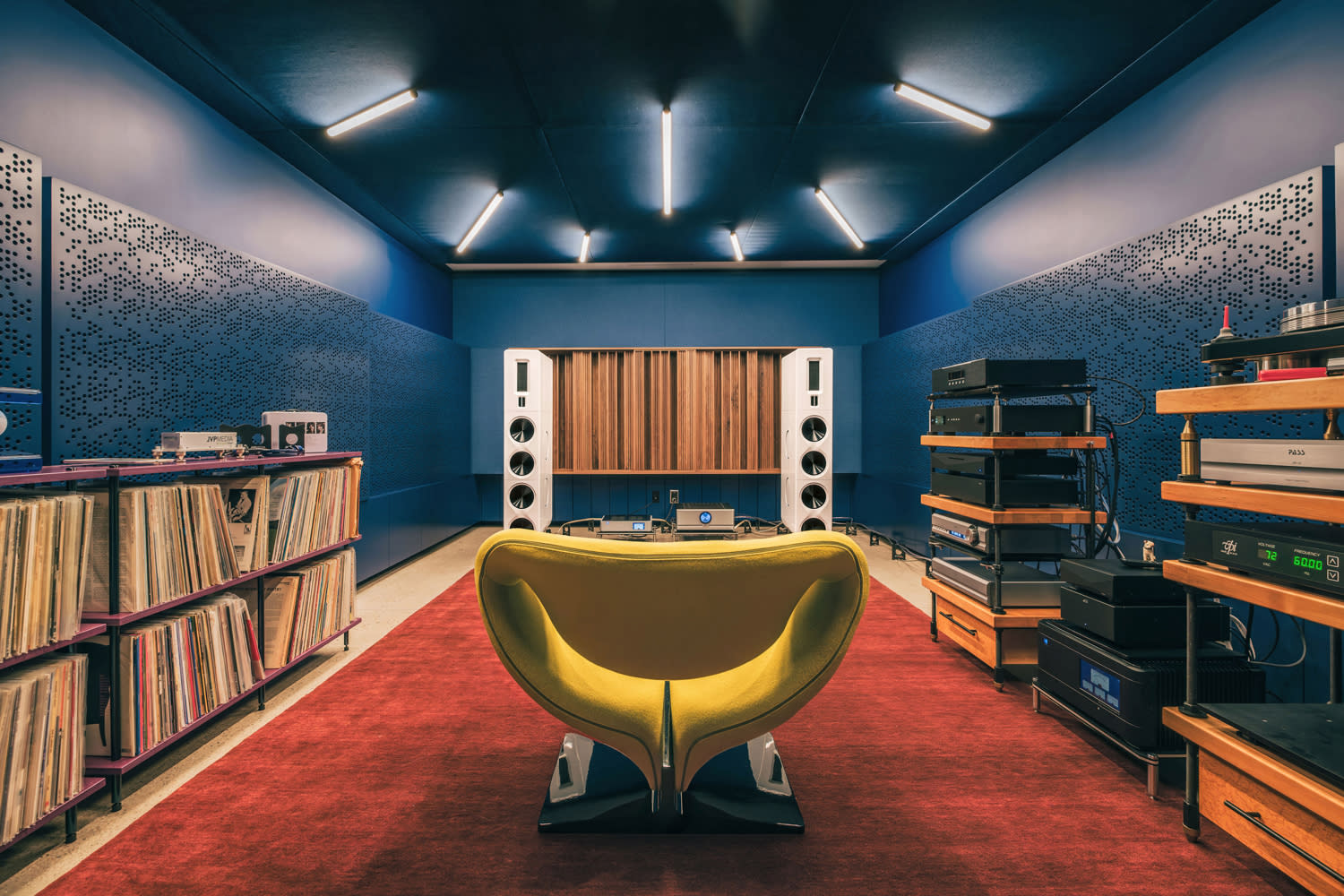 A cozy listening room with a modern yellow chair facing large speakers.