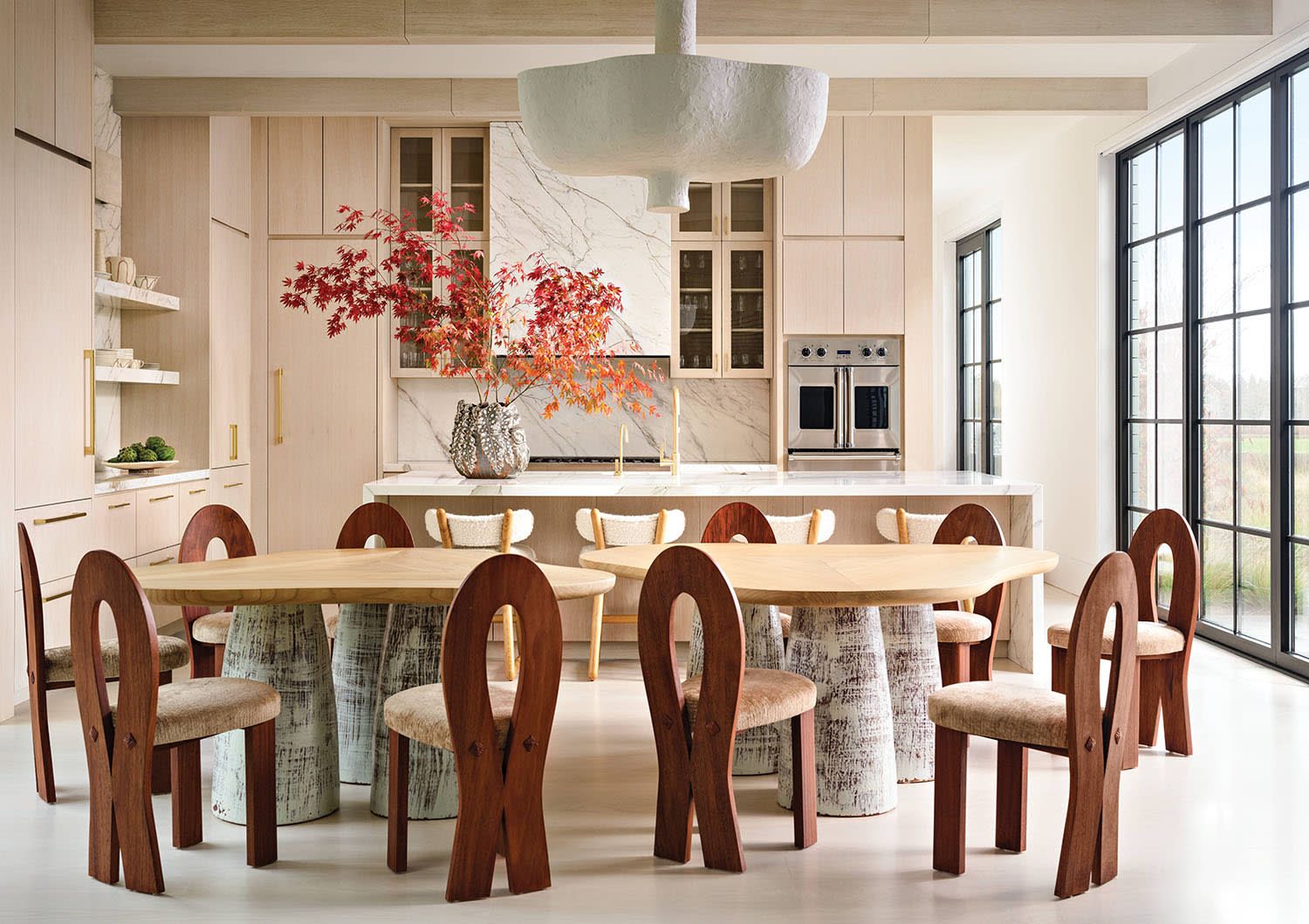 modern eat-in kitchen with double dining tables and sculptural chairs and pale pink cabinetry 