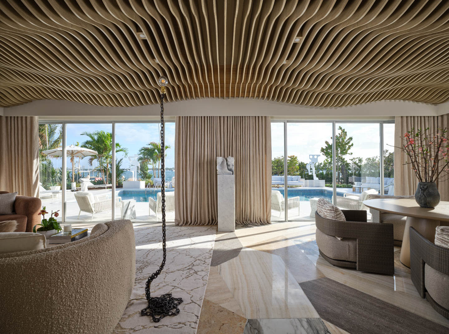 Luxurious living room with wavy wooden ceiling, marble floors, and large windows overlooking a sunny poolside. Elegant, relaxed atmosphere.