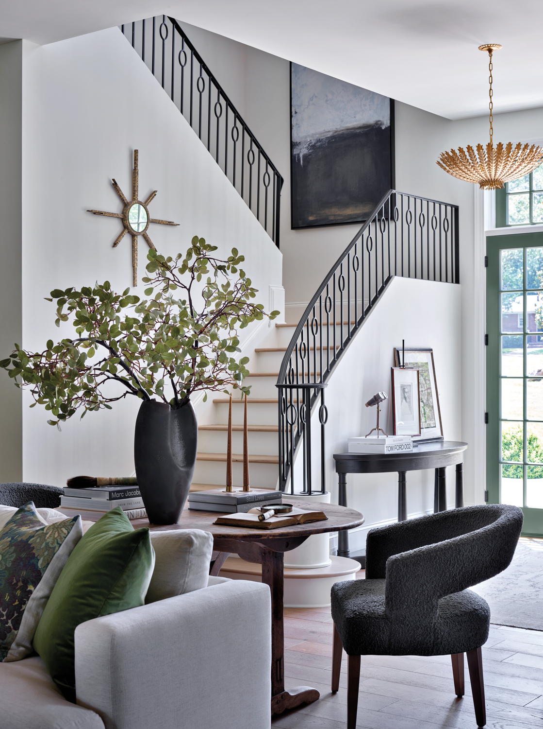 Sunlit entryway with an iron stair railing, brass ceiling pendant and greenery