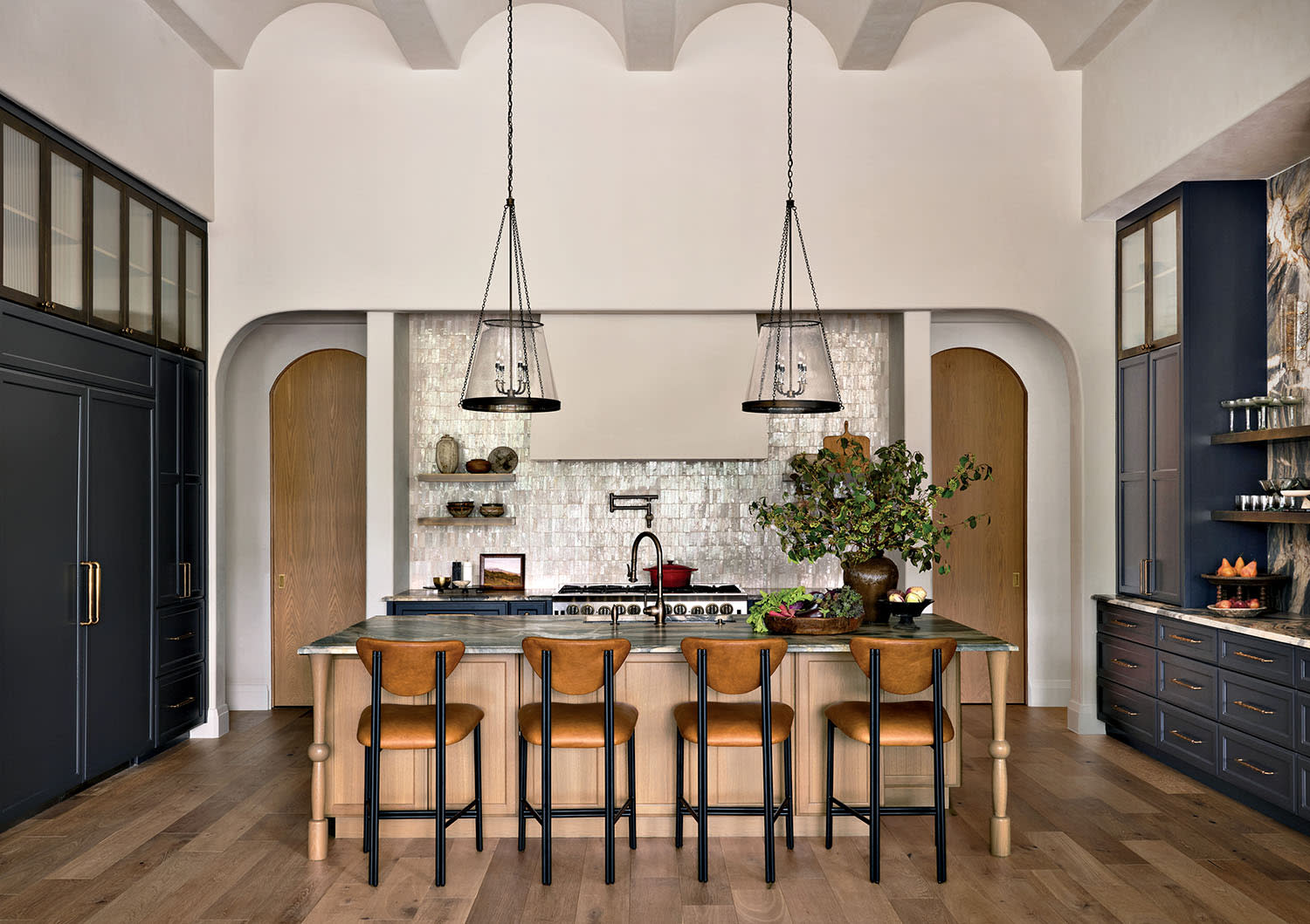 Luxurious kitchen with high ceilings, featuring a central island with five brown chairs, hanging pendant lights, and sleek dark cabinetry. Elegant and inviting.