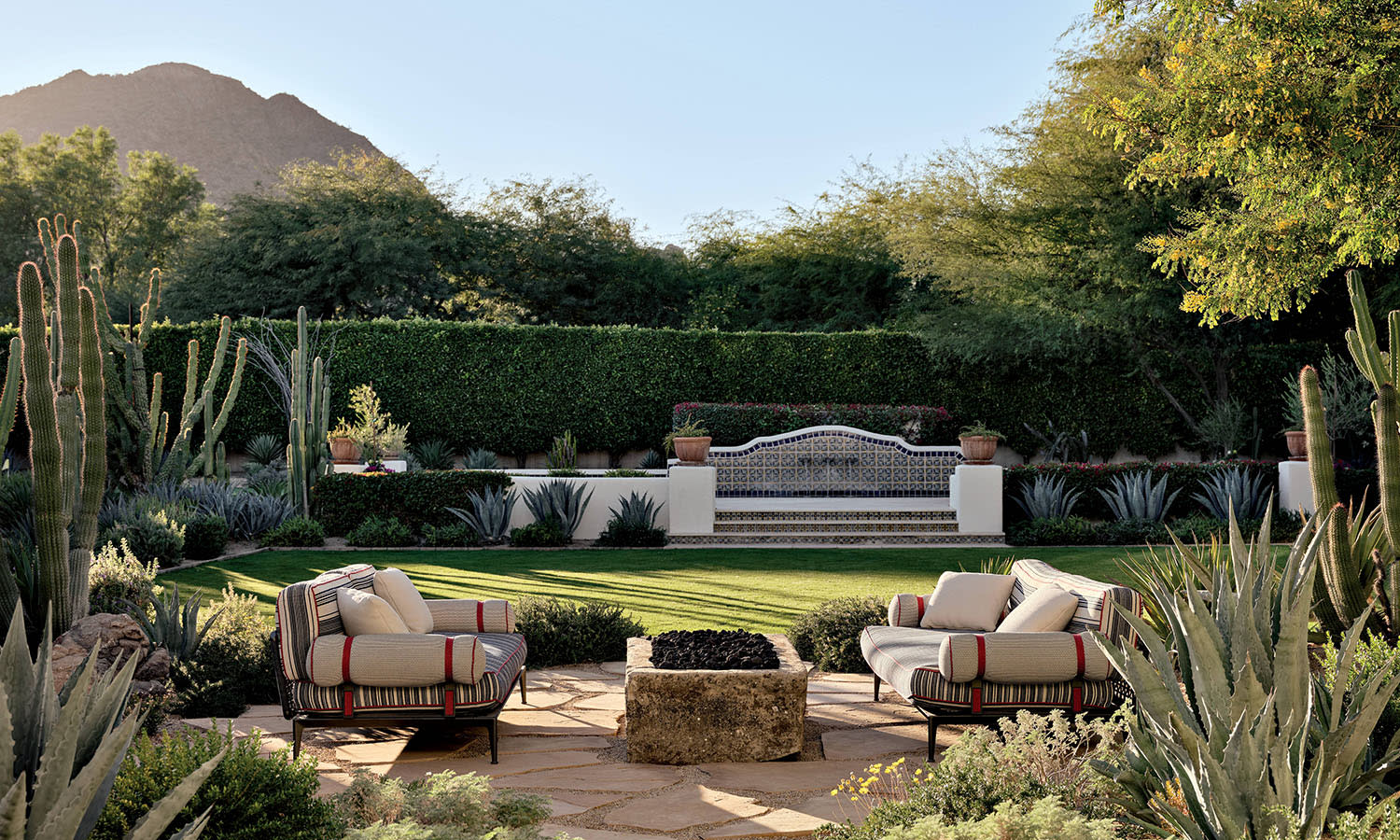 Two sofas flank a stone fire pit in a backyard filled with landscaped cacti and other greenery.
