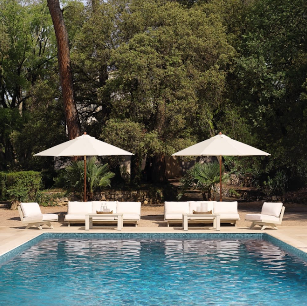 A serene outdoor setting showcasing a spacious blue pool complemented by two seating areas adorned with white umbrellas.