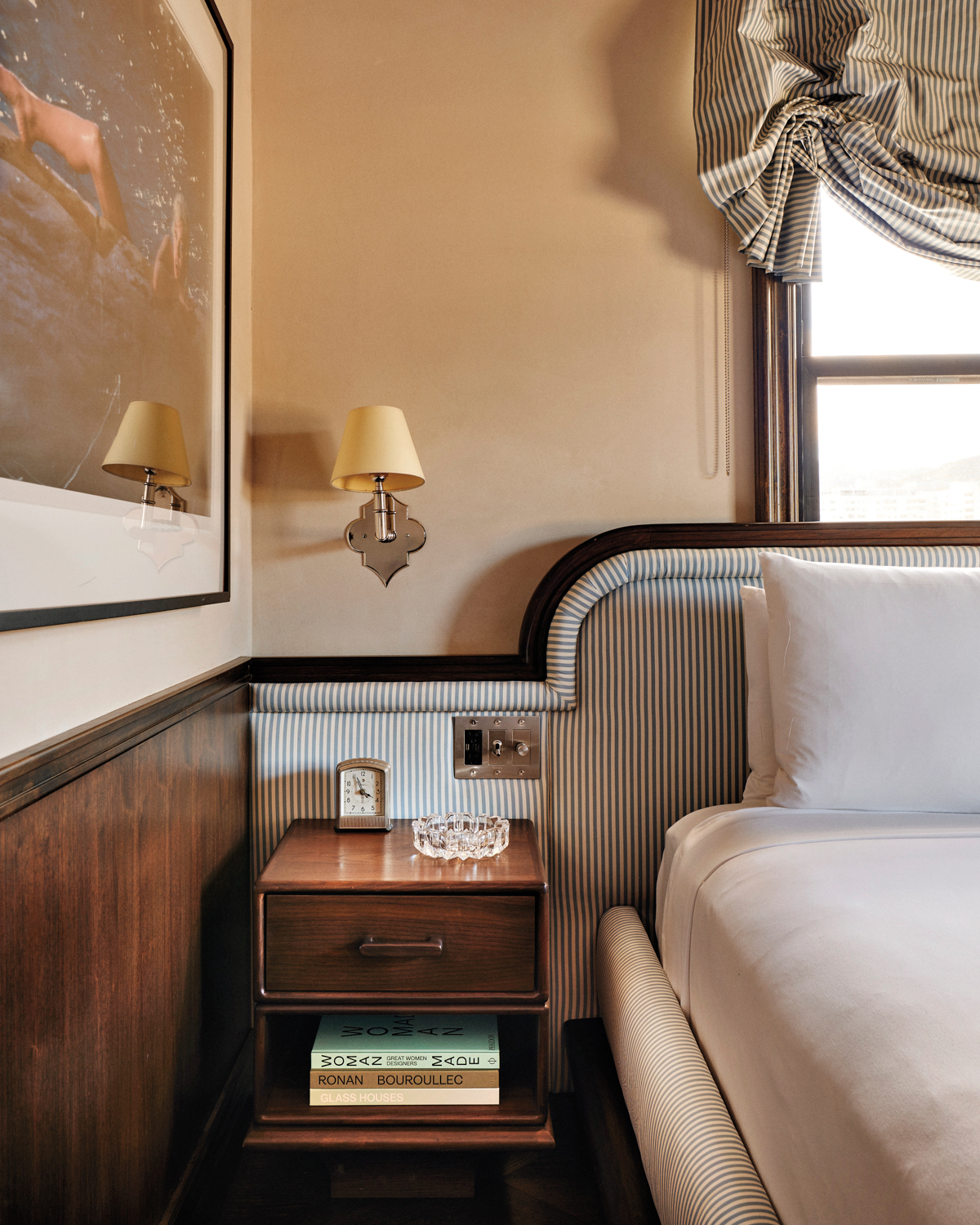 Detail of a hotel bed with a pin-stripe upholstered headboard, white beddings and a photograph of Marilyn Monroe on the wall beside. 