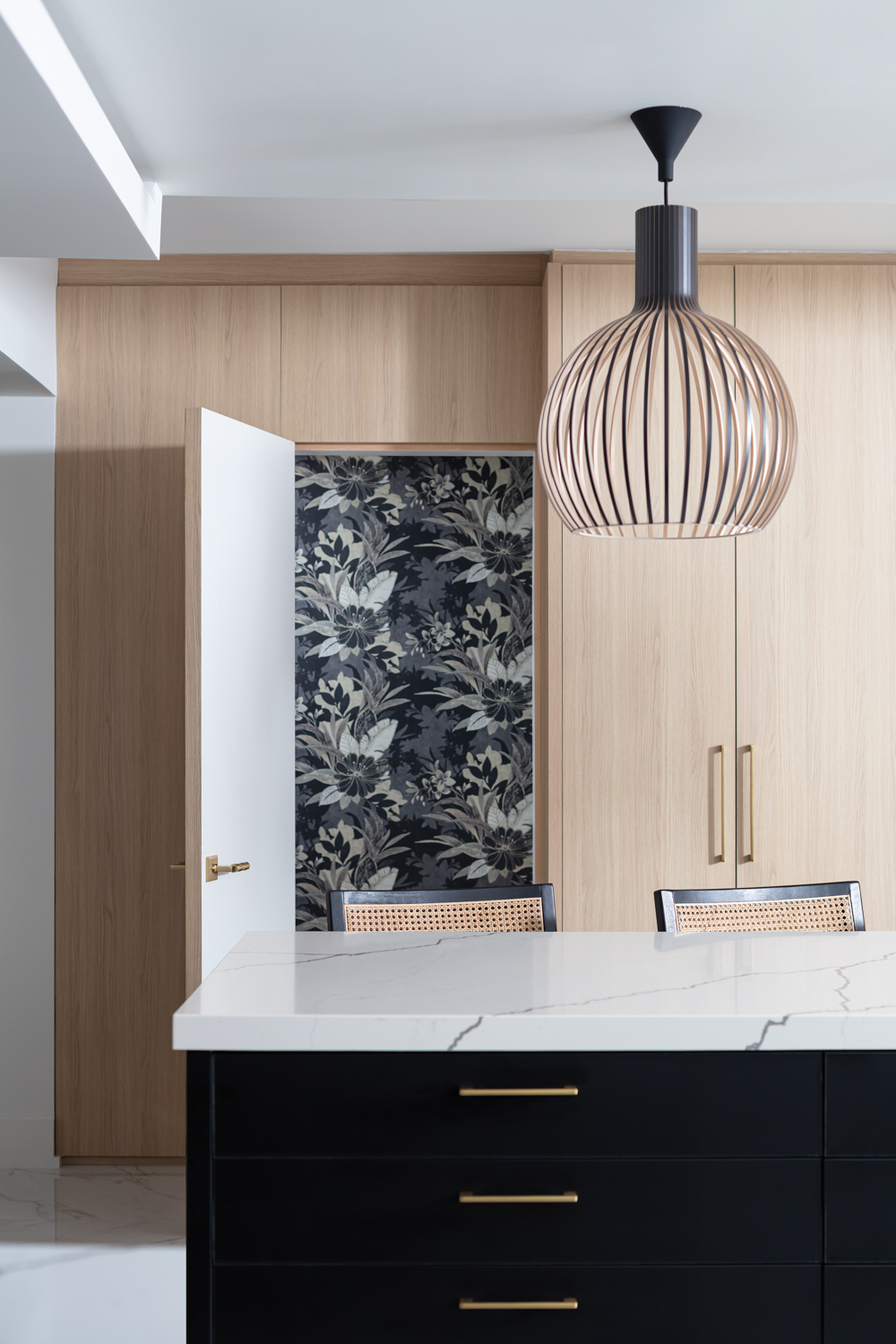 white marble topped kitchen island in front of a door to a black-and-white floral wallpapered room