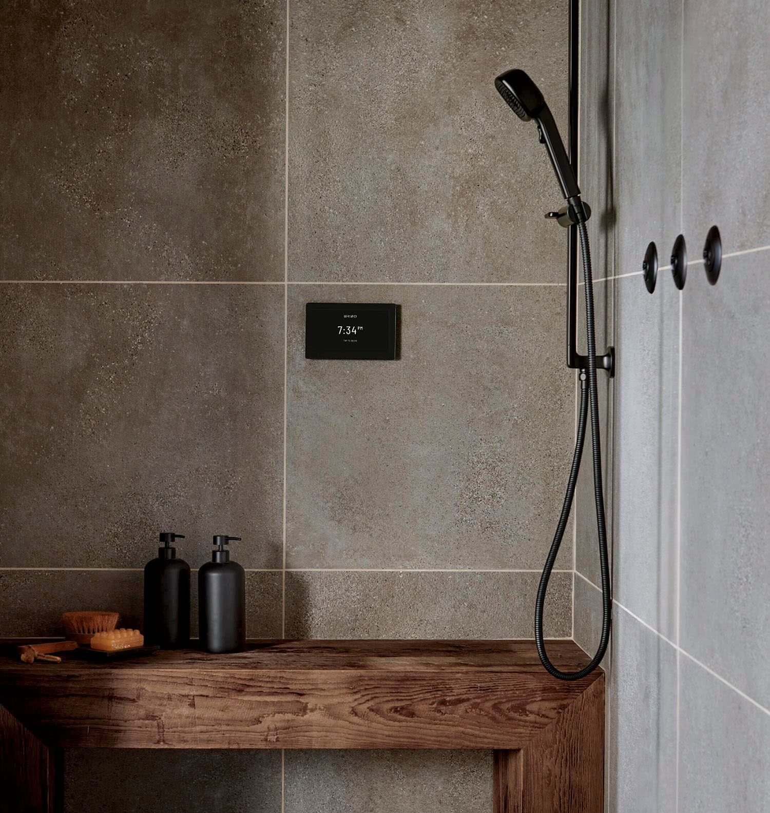 A shower with large stone tiles, a wood bench and a digital temperature system on the wall.