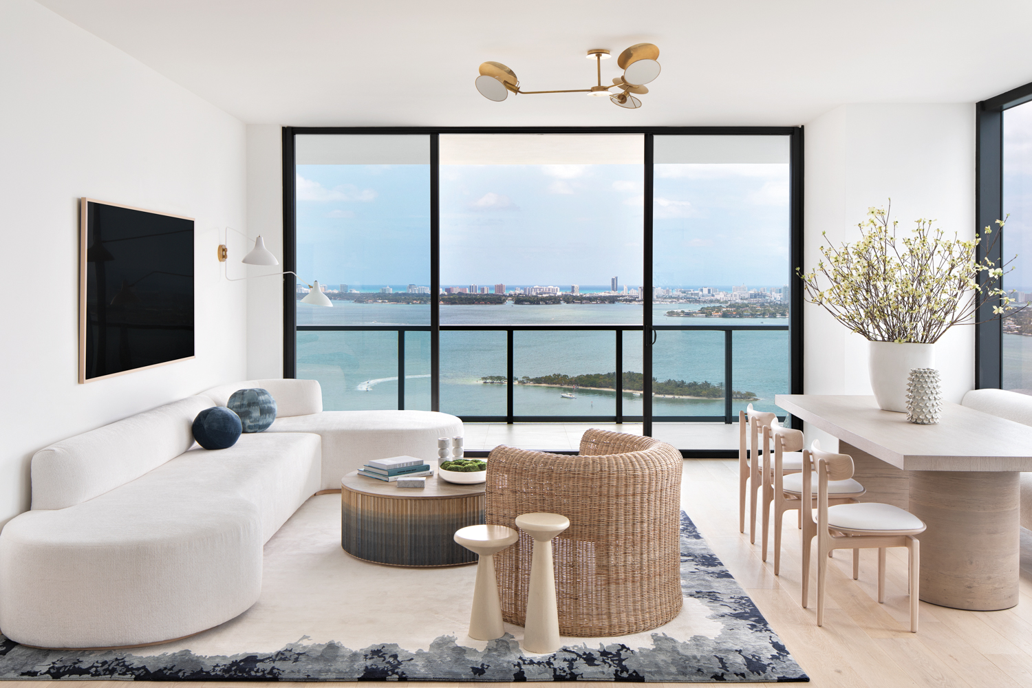 living area with white sectional, wood side tables, wicker coffee table and armchair and bordered rug