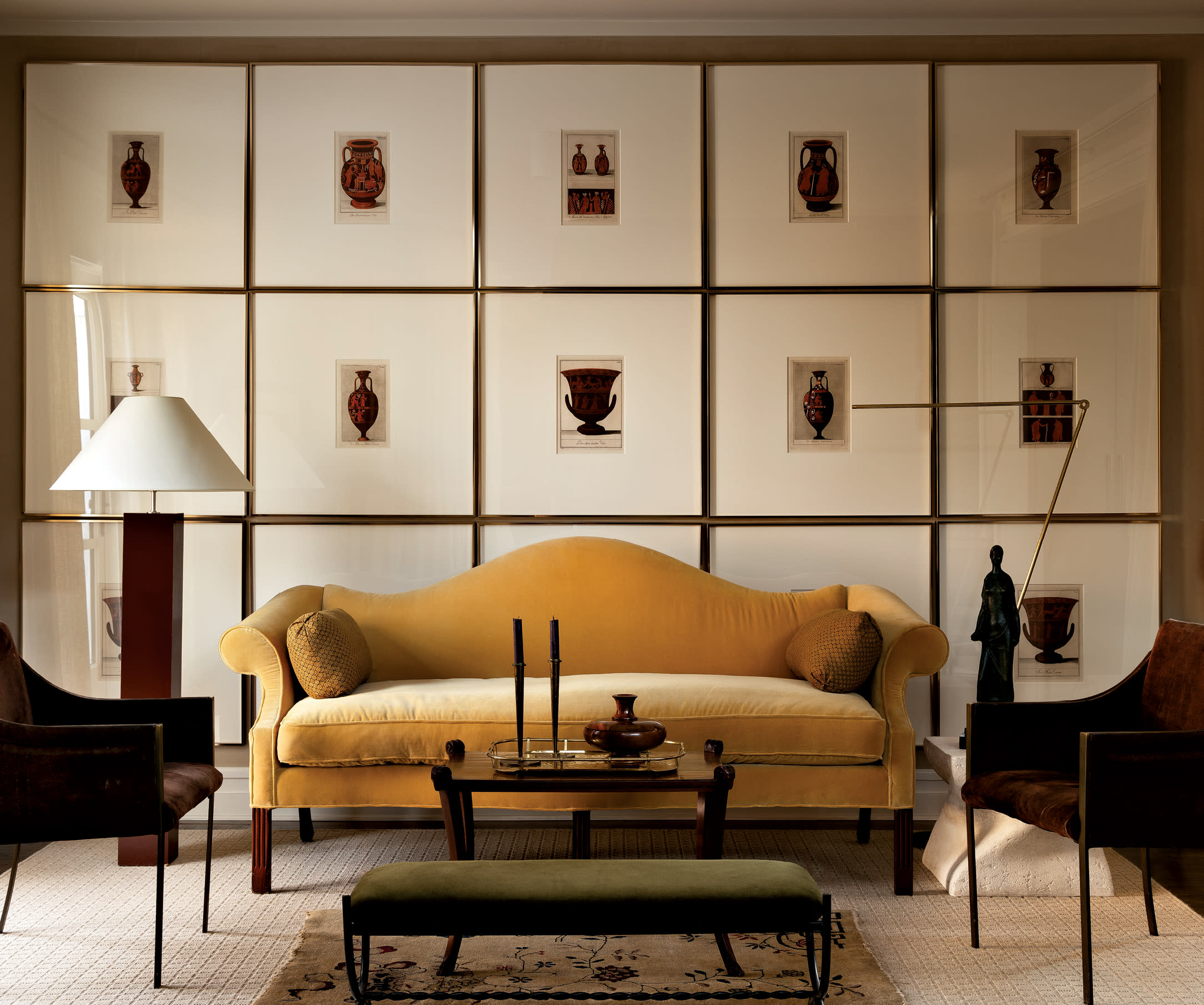 gallery wall of copper engravings behind a yellow vintage sofa flanked by French armchairs