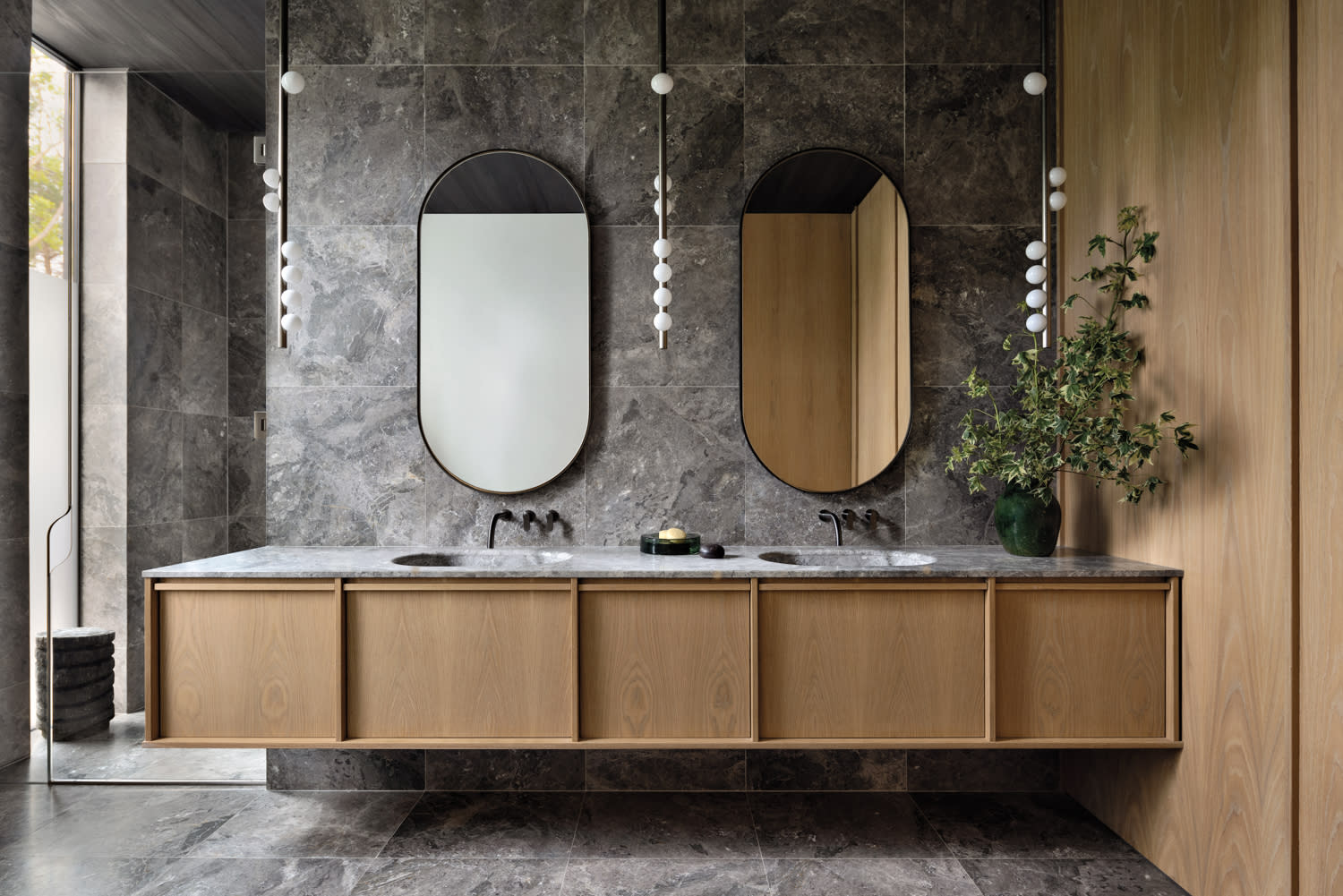 contemporary bathroom with oval mirrors and stone walls and flooring