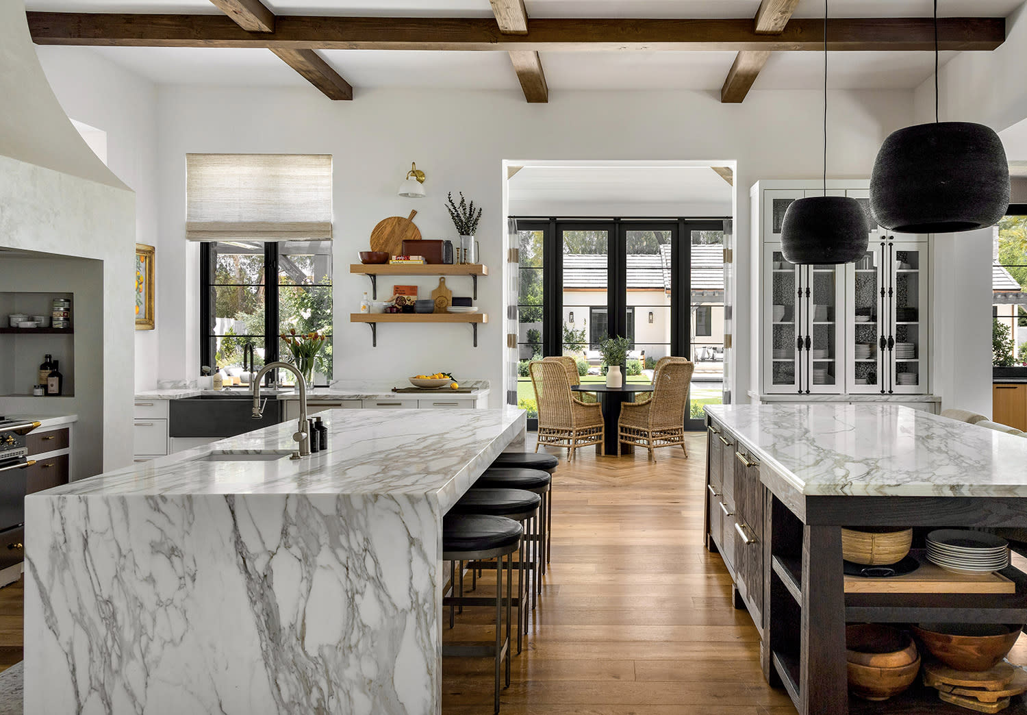 Spacious kitchen with marble countertops, wooden beams, and large windows. Black pendant lights hang above the island, creating a bright, elegant atmosphere.