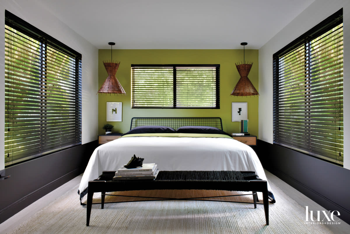 bedroom with green wall, white bed, rattan pendants and black bench