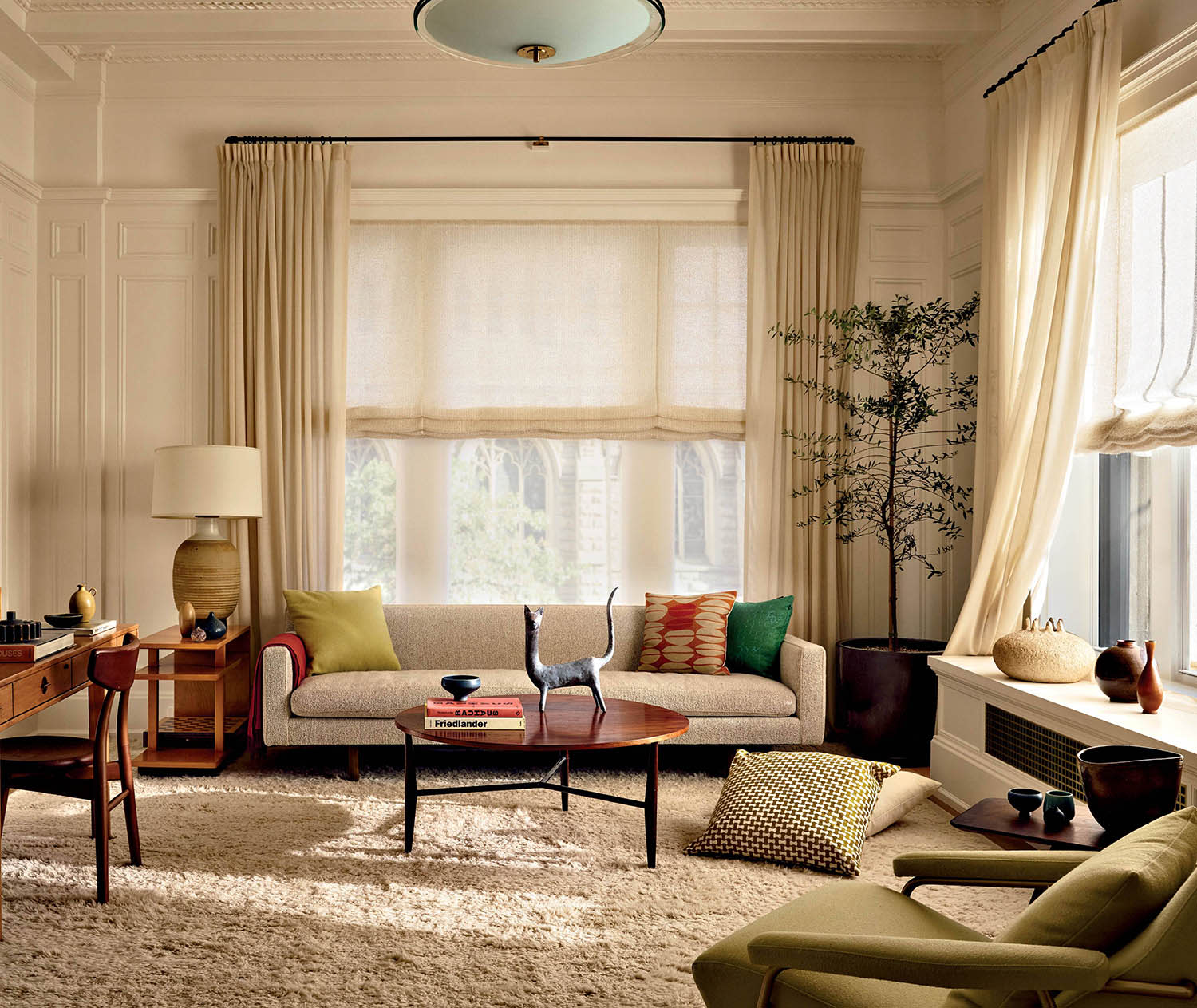 A sofa with colorful accent pillows sits against a window, with a round wood coffee table.