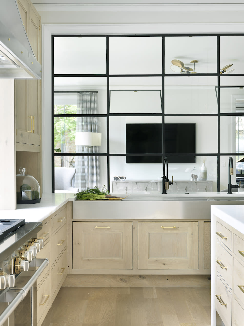 Large farmhouse with two black faucets, light cabinetry and black pane window.