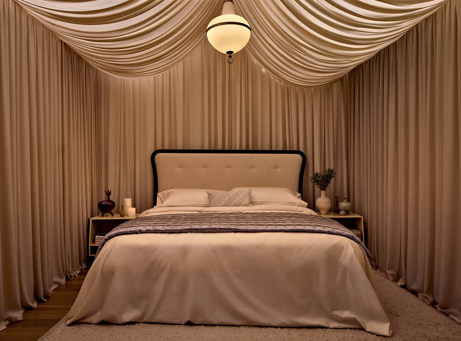 A bedroom with draped fabric lining the walls and ceiling, with an overhead light fixture over a bed.