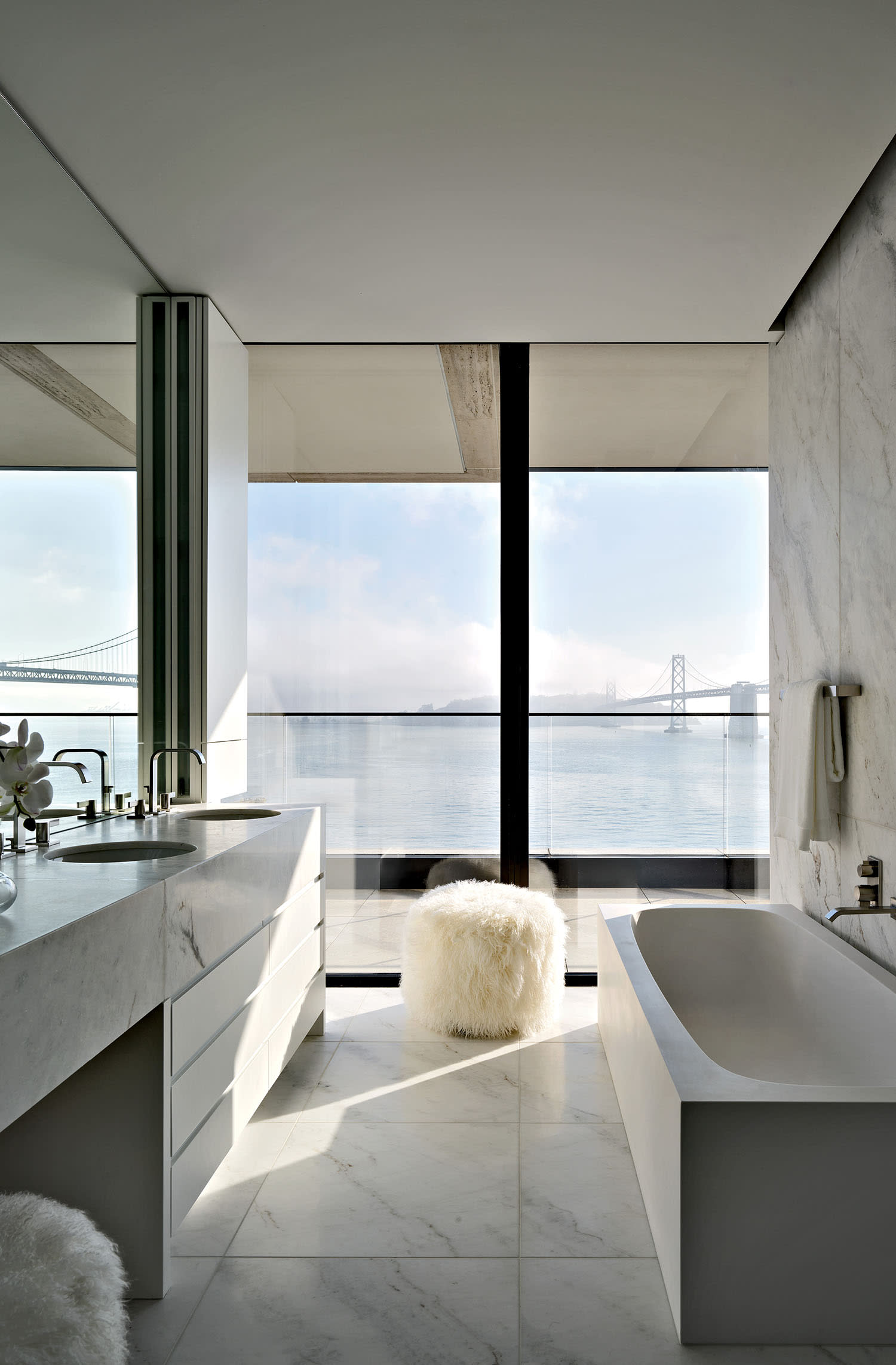 sleek bathroom with Carrara marble floors and counters and a Tibetan wool-covered pouf