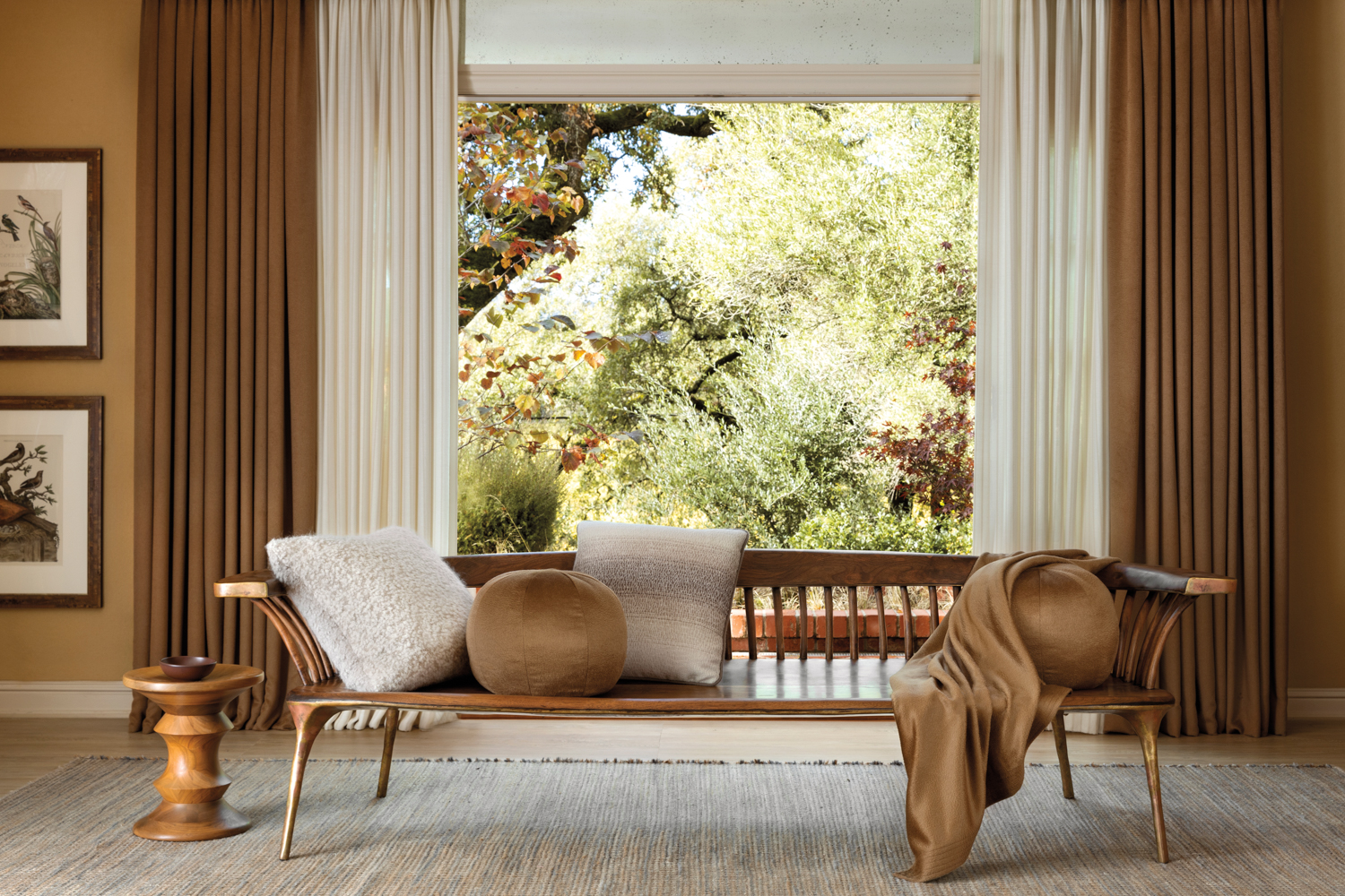 Wood bench and throw pillows atop a neutral rug in front of a large window.