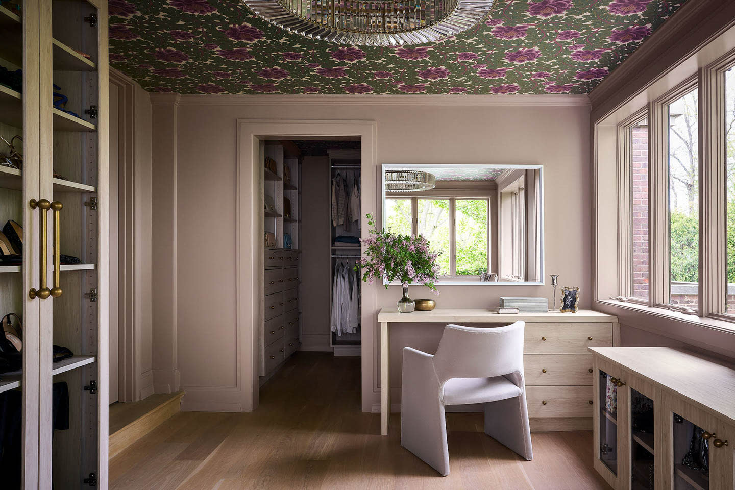 Elegant dressing room with floral ceiling, large window, vanity with flowers, and walk-in closet. Soft tones, neatly organized, serene atmosphere.