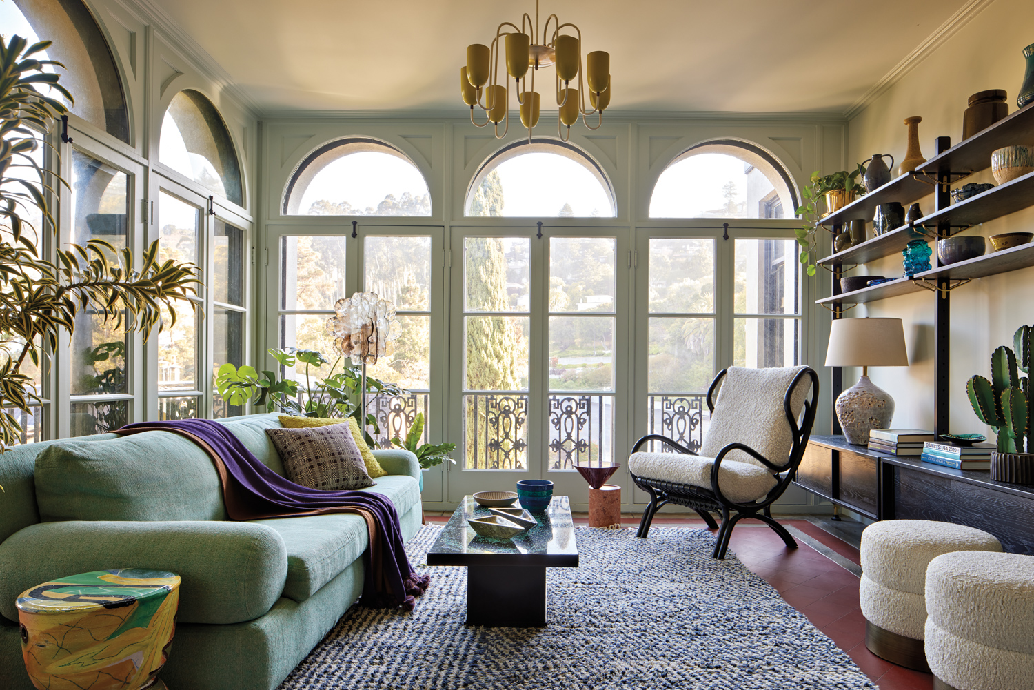 Sun room with large arched windows, chandelier, green vintage sofa, and white armchair