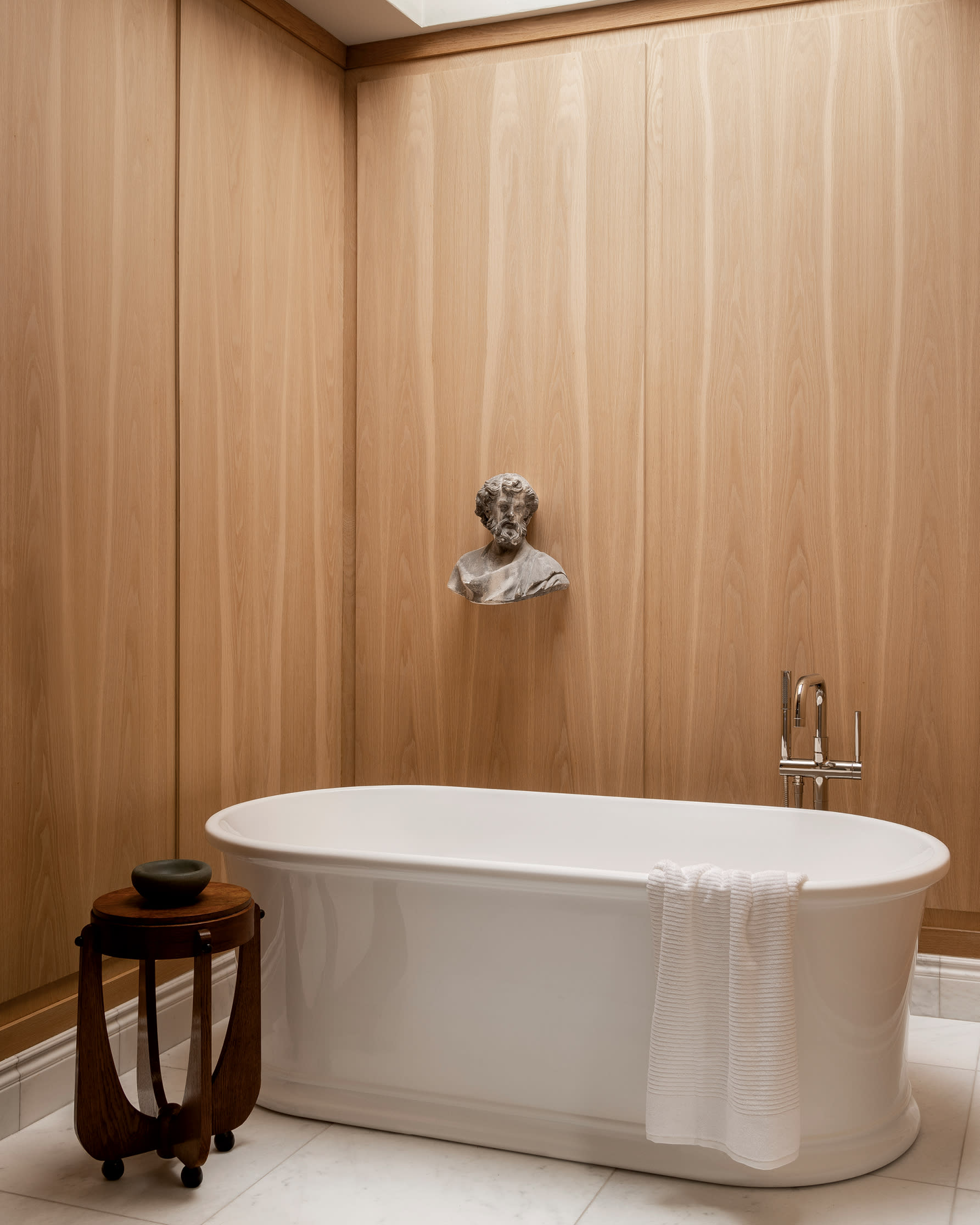 bathroom with white oak paneling and a plaster bust on hanging above the bathtub