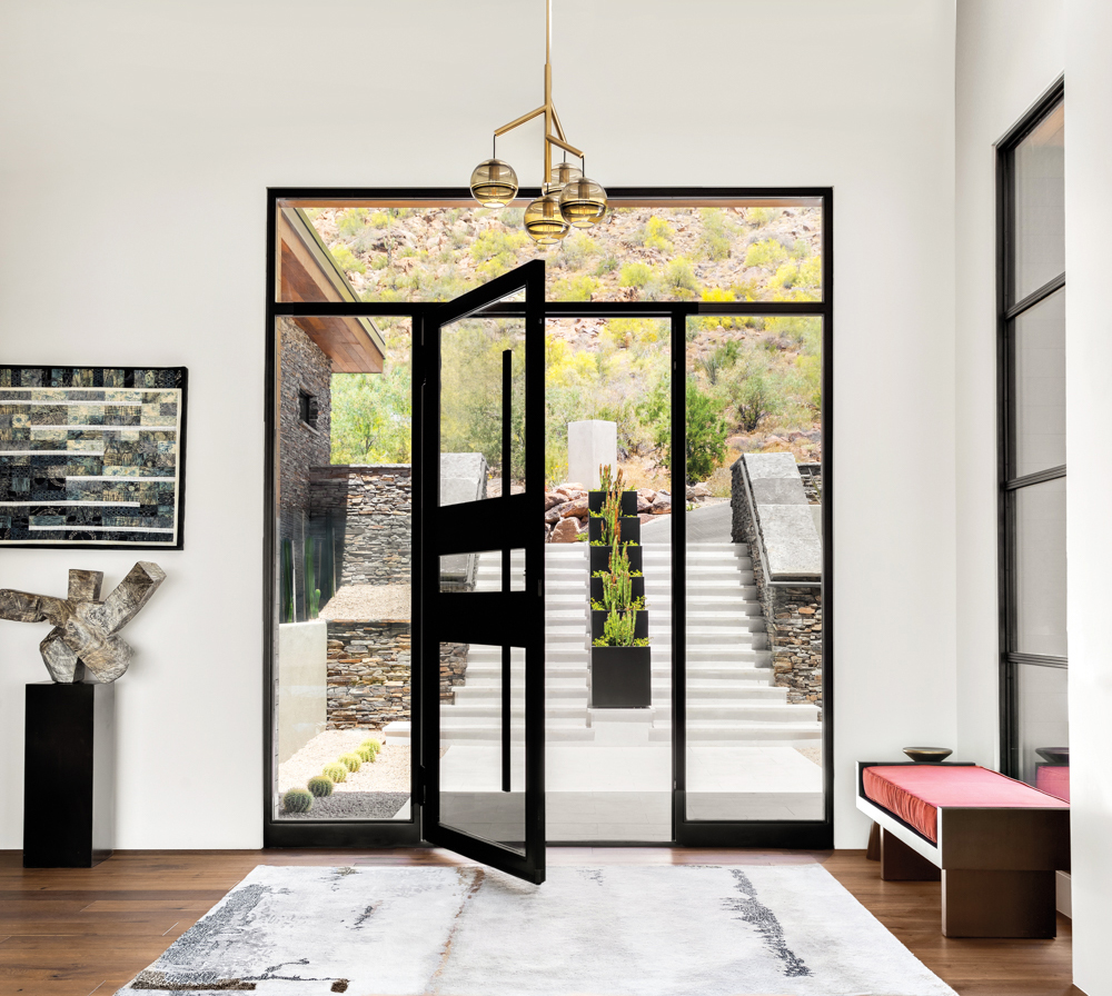 black steel and glass door opens to an entry with a red bench, abstract painting and stone sculpture